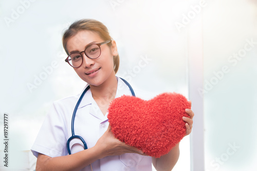 woman doctor holding red heart, asian doctor holding red heart pillow and blue stethoscope necklet in office or working room