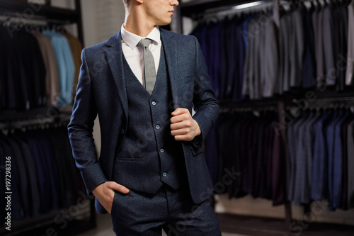 sale, shopping, fashion, style and people concept - elegant young man choosing and trying jacket on in mall or clothing store