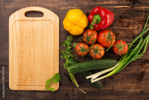 Various vegetables and empty cutting board. Colorful ingredients for cooking on rustic wooden table around empty cutting board with copyspace. Top view.