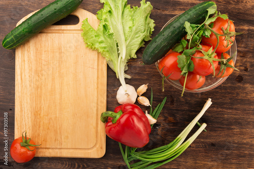 Various vegetables and empty cutting board. Colorful ingredients for cooking on rustic wooden table around empty cutting board with copyspace. Top view.