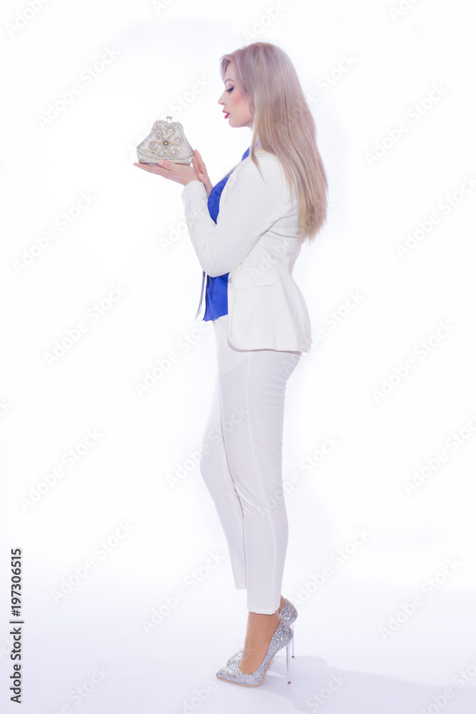 Studio portrait in full length of a beautiful young blond woman with long hair in a white pants suit. A girl in silvery shoes with high heels, in her hands she holds a small silver handbag Studio portrait in full length of a beautiful young blond woman with long hair in a white pants suit. A girl in silvery shoes with high heels, in her hands she holds a small silver handbag
