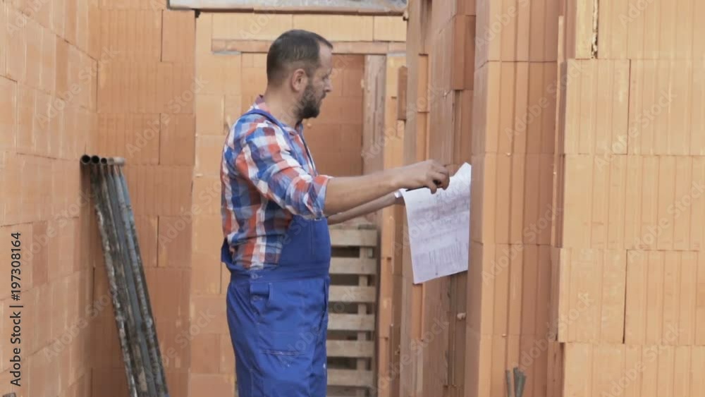 Young male worker with blueprints and measure tape checking home at construction site
Young male worker with blueprints and measure tape checking home at construction site