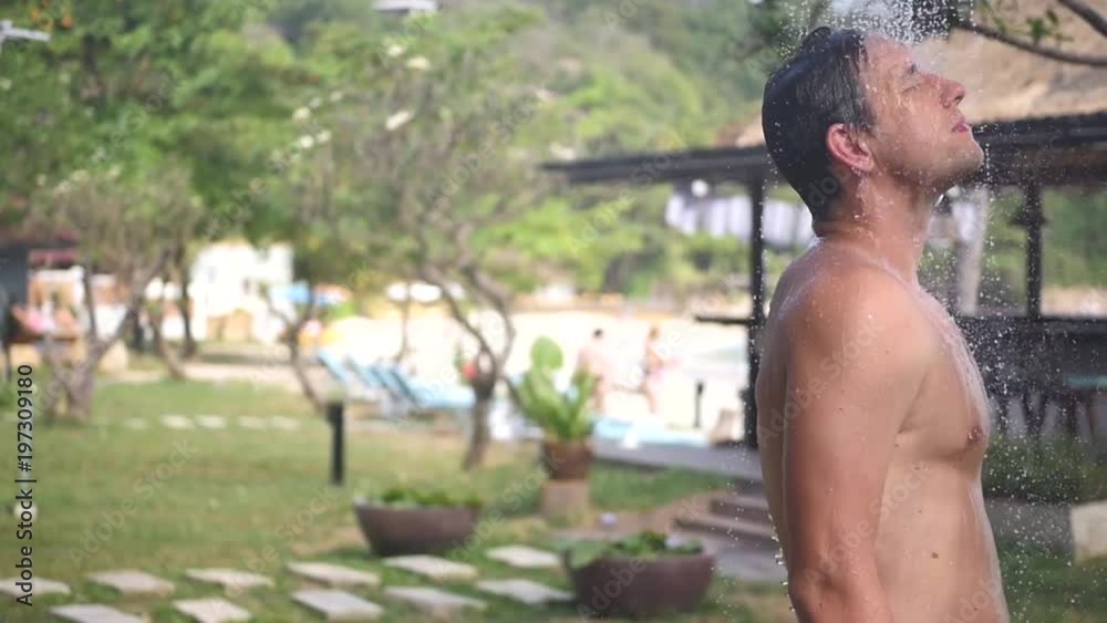 An attractive man is standing under a shower under the open sky, on the beach. slow motion, 1920x1080, full hd An attractive man is standing under a shower under the open sky, on the beach. slow motion, 1920x1080, full hd