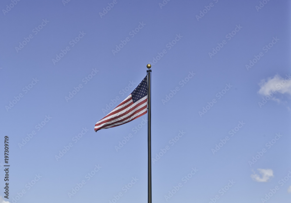An American flag on a black metal pole weaving in the clear sky on the 4th of July. Stars and stripes on a background ideal for copyspace. Concept for independence, freedom and patriotism An American flag on a black metal pole weaving in the clear sky on the 4th of July. Stars and stripes on a background ideal for copyspace. Concept for independence, freedom and patriotism