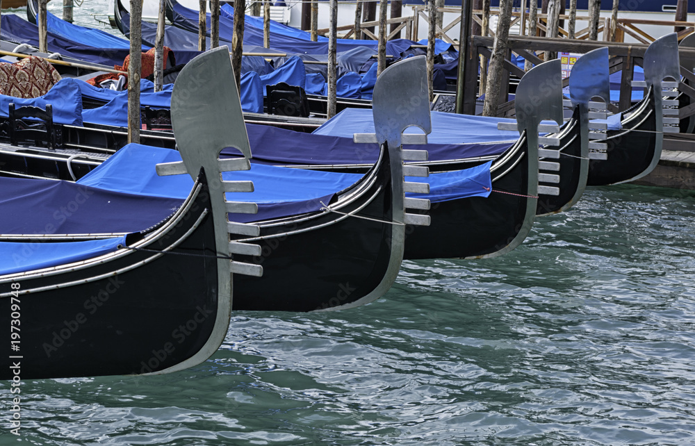 Detail on the steel prow of a Venetian gondola moored in the canal in front of San Marco square in Venice. The gondola is a traditional flat-bottomed boat similar to a canoe. Unesco
