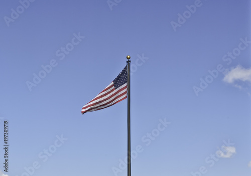 An American flag on a black metal pole weaving in the clear sky on the 4th of July. Stars and stripes on a background ideal for copyspace. Concept for independence, freedom and patriotism
