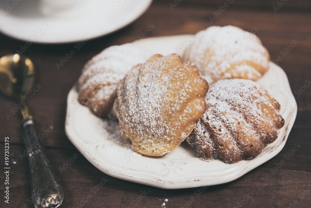 Homemade french madeleines with beurre noisette and cup of coffee on wooden table. Horizontal. Homemade french madeleines with beurre noisette and cup of coffee on wooden table. Horizontal.