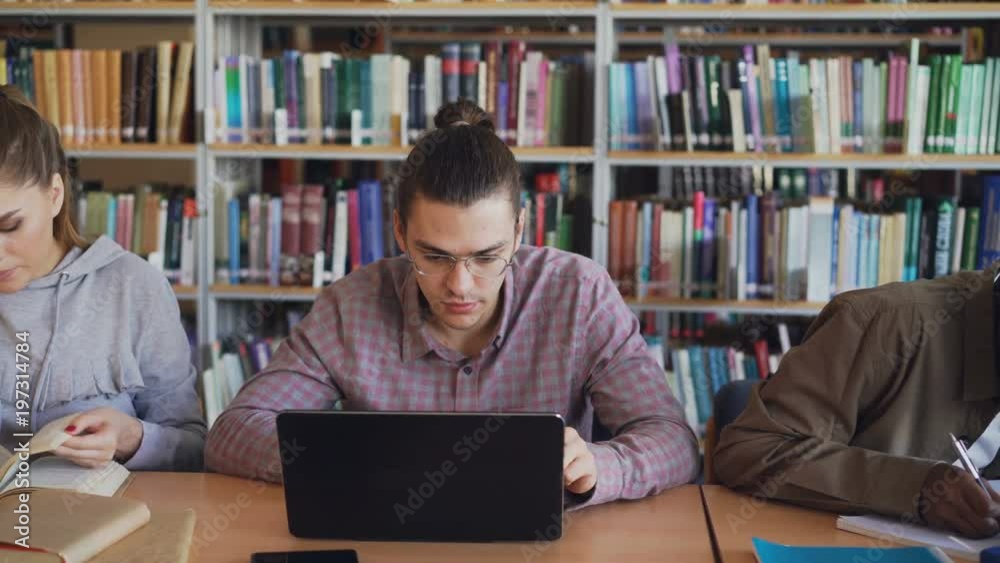 Pan shot of Multi ethnic group of concentrated students preparing for examination while sitting at table in university library Pan shot of Multi ethnic group of concentrated students preparing for examination while sitting at table in university library