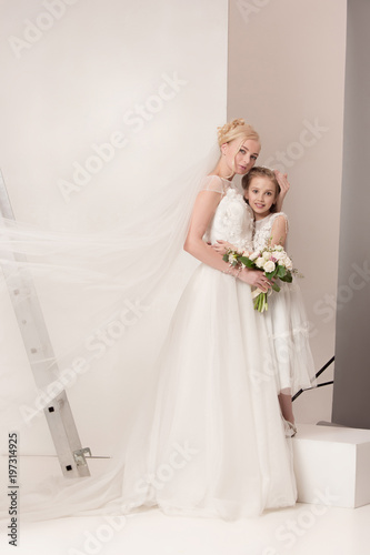 Little pretty girls with flowers dressed in wedding dresses