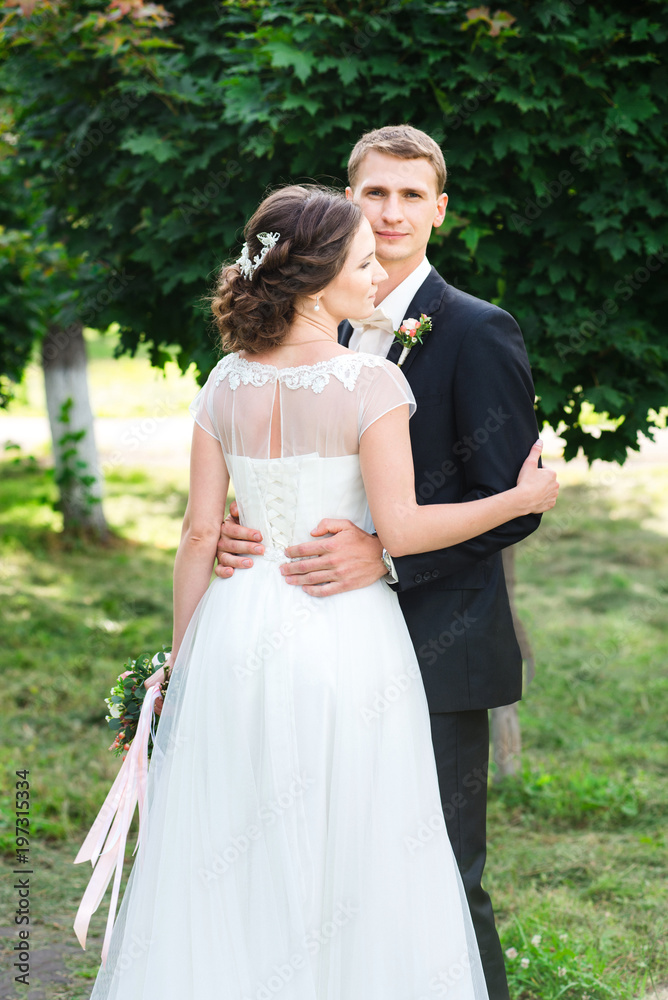 Young couple just married. Wedding couple hugging gently in a green garden, the bride standin back to the shot Young couple just married. Wedding couple hugging gently in a green garden, the bride standin back to the shot