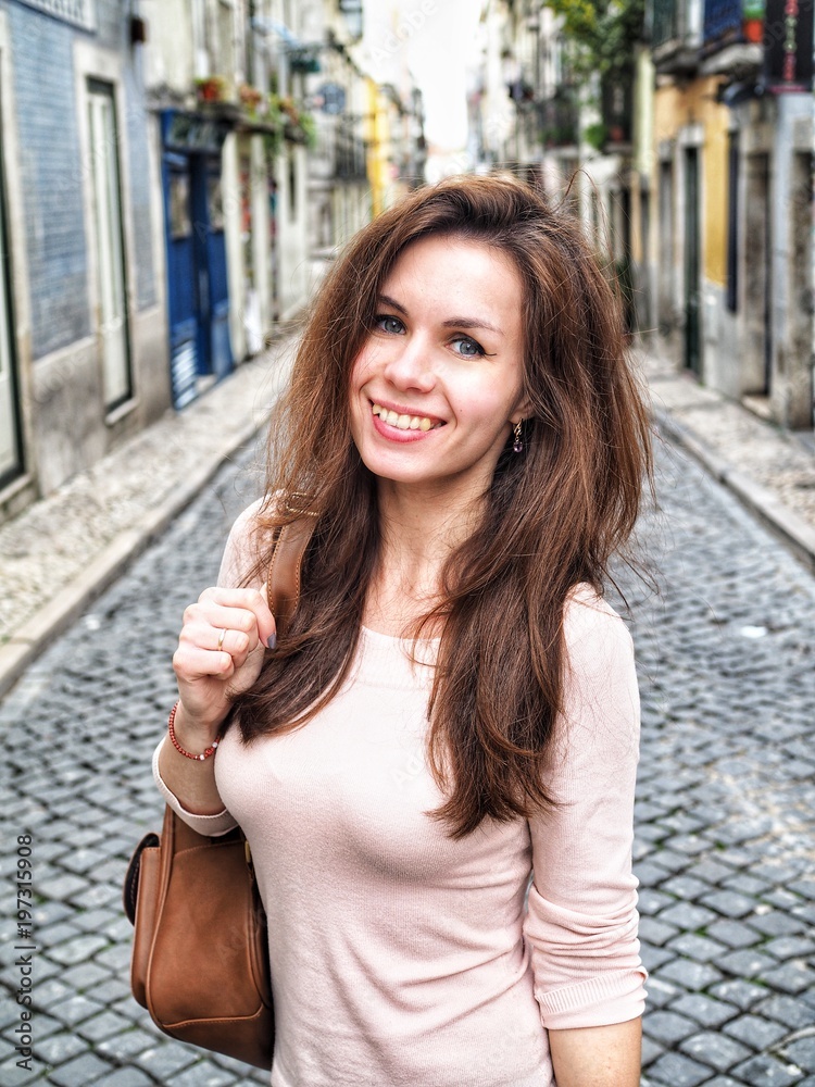 Girl with long hair smiling standing in front of empty narrow European street in Portugal