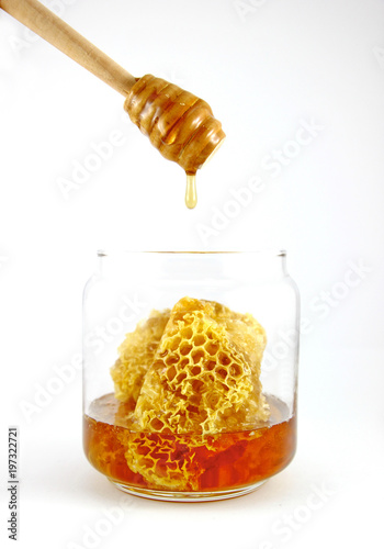 Honey dipper with fresh honey and honeycomb in glass jar on a white background