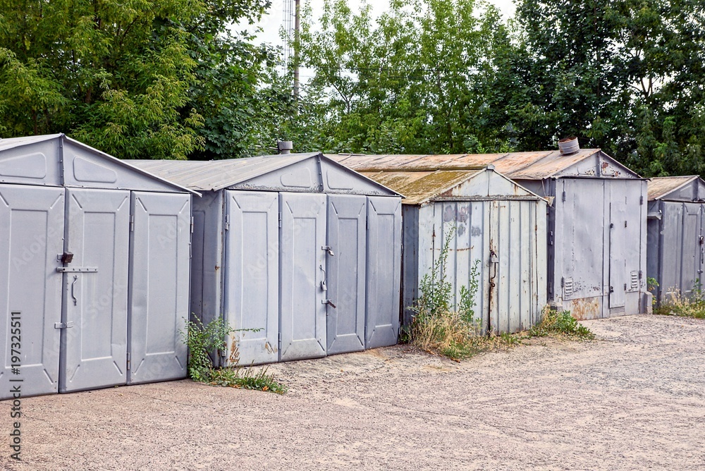 Old gray iron garages in the thickets of grass near the road