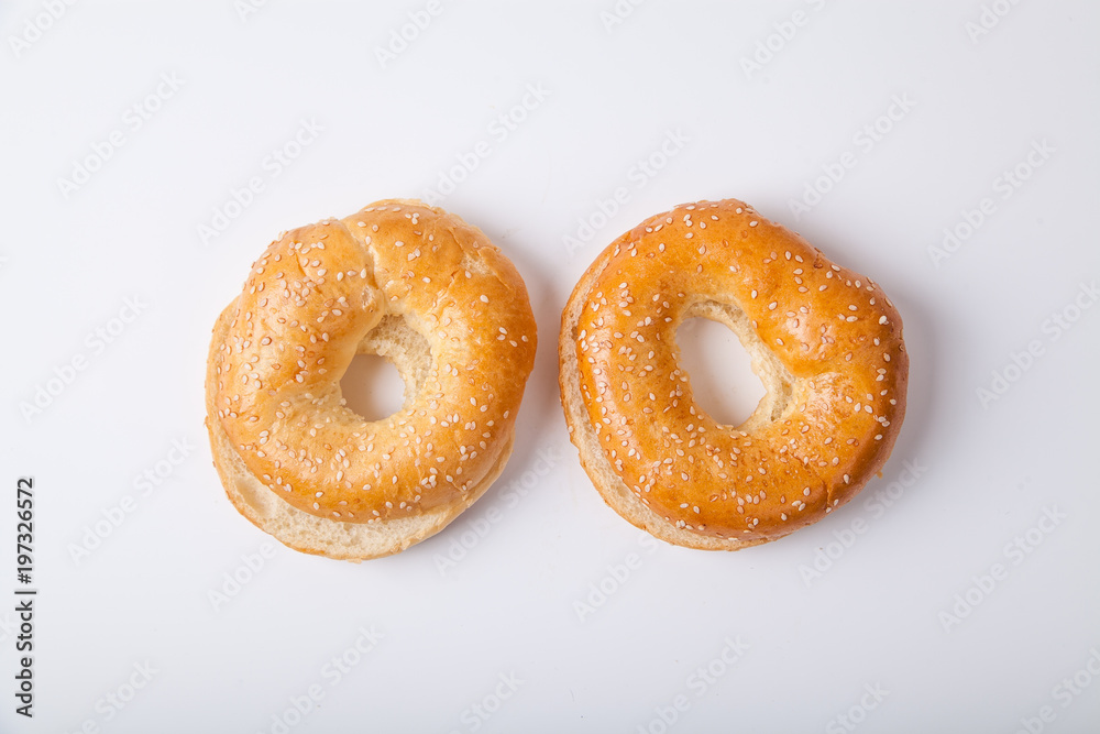 Two fresh baked bagle buns with sesame seeds on white background pre-cut for making sandwiches