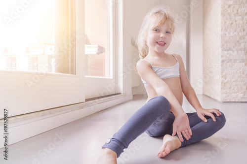 Happy little blond girl in white top and blue leggings sitting on the floor  in the sunny room foto de Stock | Adobe Stock