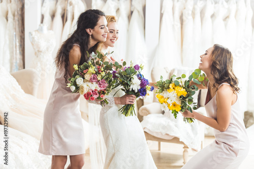 Young bride and bridesmaids holding tender flowers bouquets in wedding atelier