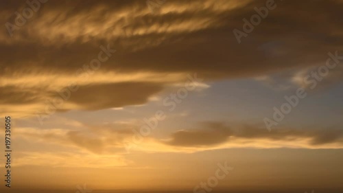 	 4k time lapse of clouds crossing the amazing sky over the sea or ocean at sunset. transition from day to night. The clouds cross slowly from left to right colored yellow orange purple blue.