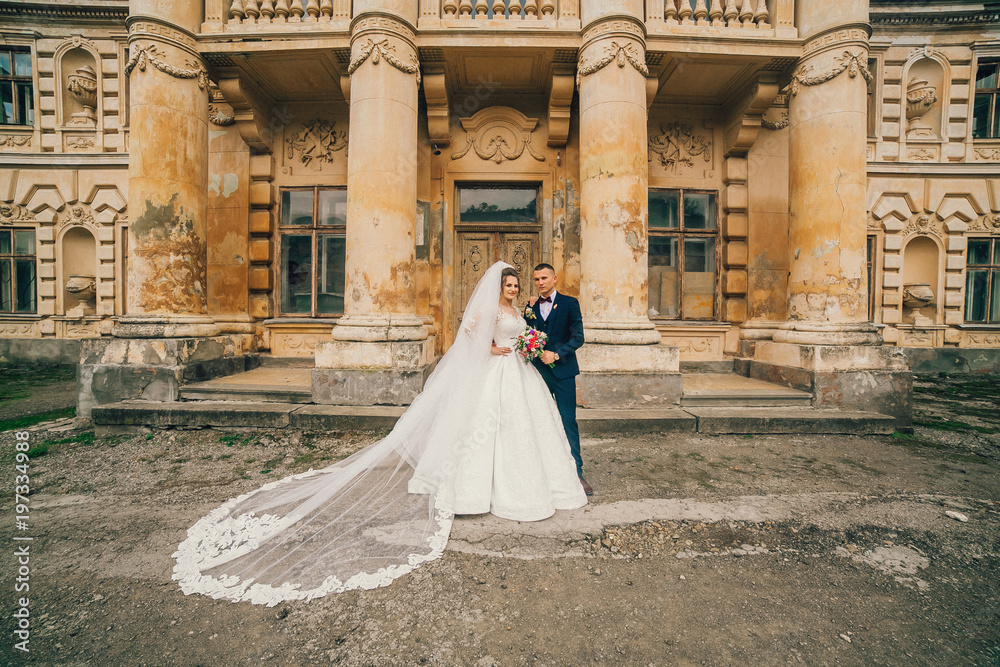 Beautiful romantic wedding couple of newlyweds hugging and kiss each other near old castle with columns and ancient door