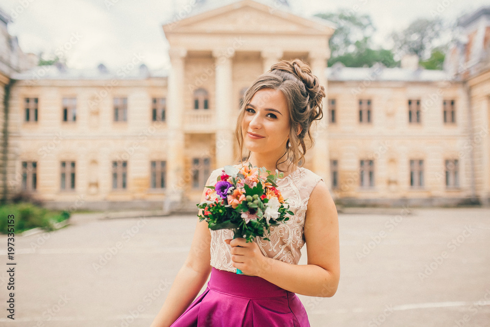 Fototapeta premium Portrait of a beautiful bridesmaid posing with bride's wedding bouquet near old castle. Amaizing wedding day.