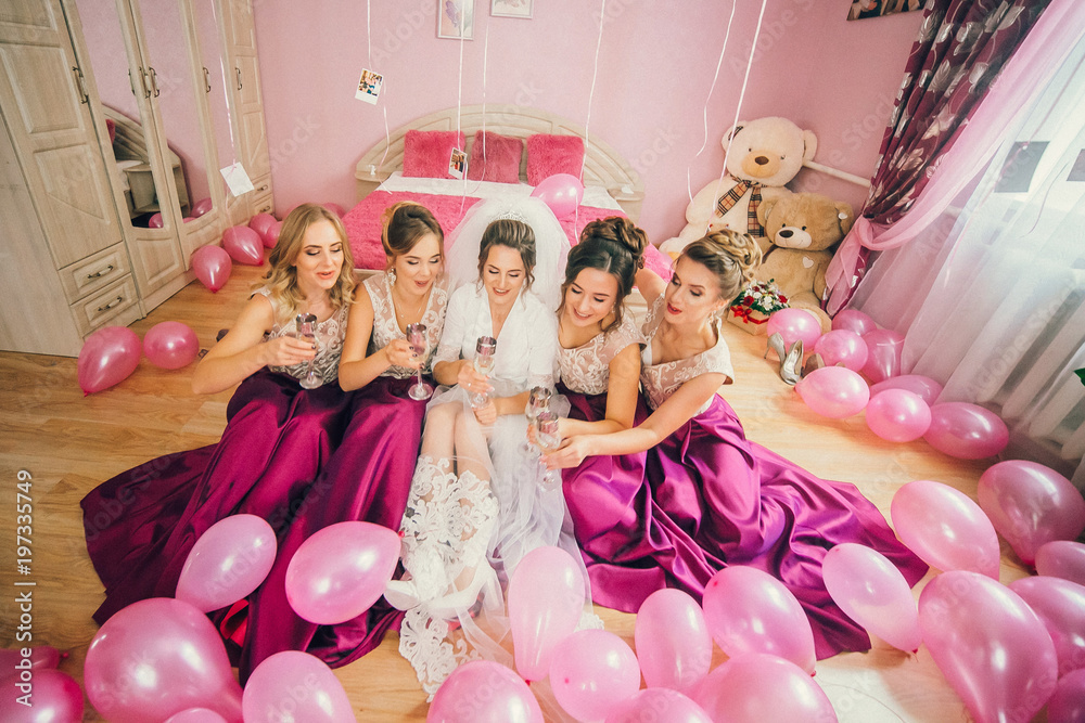 Bride and bridesmaids on the wedding day sitting on the floor with glasses of champagne. A lot of pink balloons around the Bride and bridesmaids. Amazing wedding morning.