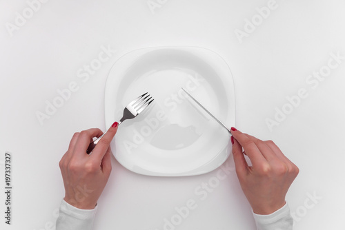Hands with cutlery over empty plate.