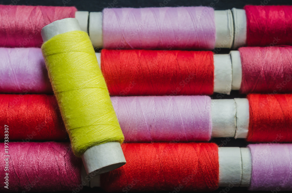 Spool of yellow thread on the background of spools of pink and red thread Spool of yellow thread on the background of spools of pink and red thread