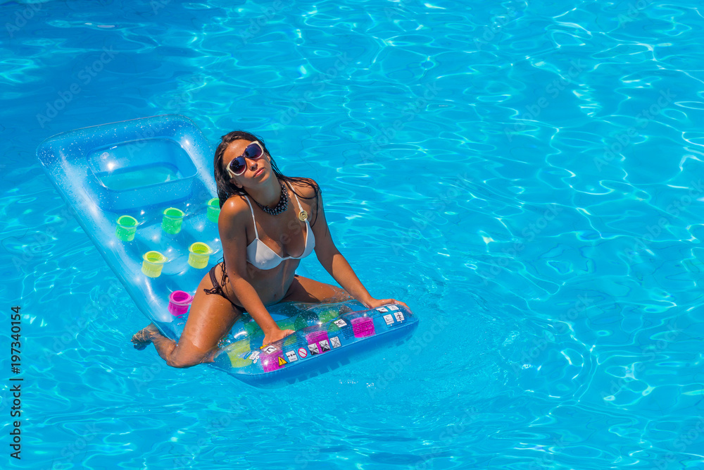 portrait of pretty young woman in swimsuit lying on a inflatable mattress at pool.