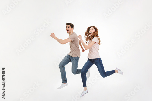 Full-length photo of energetic couple man and woman in casual t-shirt running and smiling on camera with happy look, isolated over white background