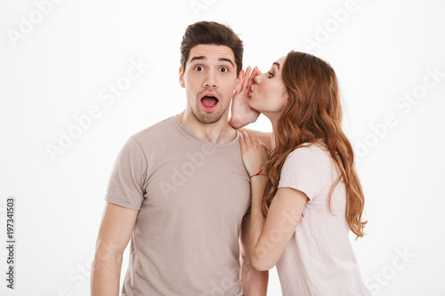 Photo of gorgeous woman with beautiful auburn hair talking secrets in ear of her boyfriend or male friend, isolated over white background