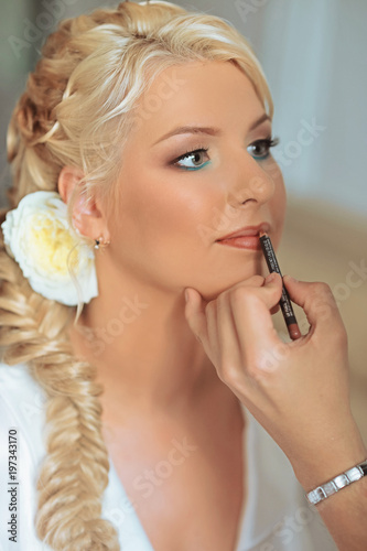 Wedding makeup artist making a make up for beautiful blonde young bride.Sexy model girl indoors. Beauty woman with curly hair. Female portrait. Bridal morning of a cute lady. Close-up hands near face