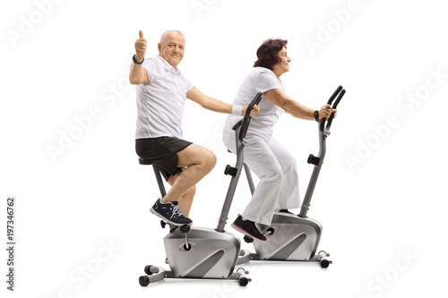 Mature man and a mature woman on exercise bikes with the man making a thumb up sign