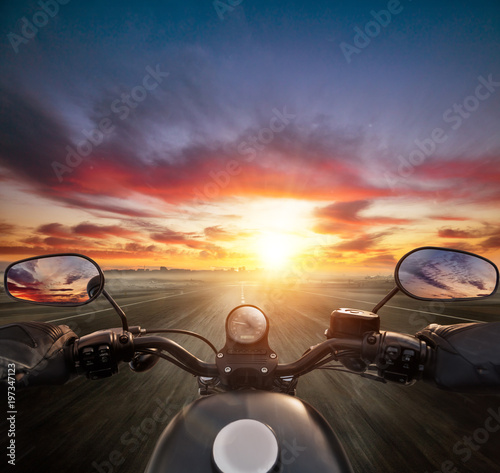 POV of motorcycle driver holding handlebar, heading to modern city skyline.