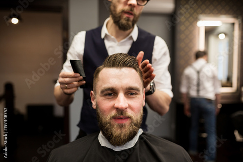 Glad young man having hair cut at barber salon