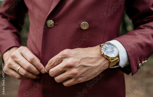 Close-up of man wearing suit and golden watch buttoning jacket