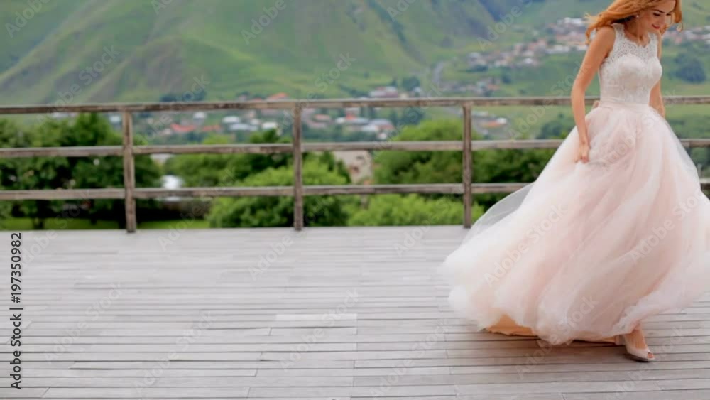 Beautiful red-haired bride dancing against the background of mountains on the open terrace. Georgia. Kazbegi.