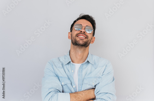 Handsome male model wearing trendy round mirror sunglasses and blue shirt having pleasant smile and white teeth posing against white background enjoy summer weather.People, lifestyle, emotions concept