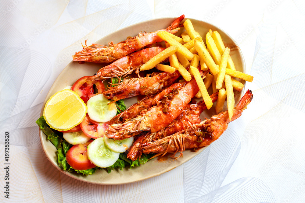 Plate grilled spicy prawn shrimps kebabs, vegetables, french fries with sauces and greens on light background.