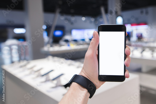 A person holds a smartphone in the background of a technology store. Phone against the background of a blurry store