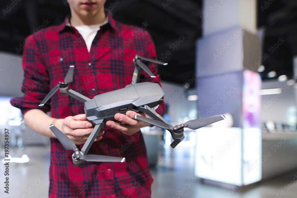 A man stands in a technology store and holds a quadcopter in his hand. Buying a quadcopter in the electronics store.
