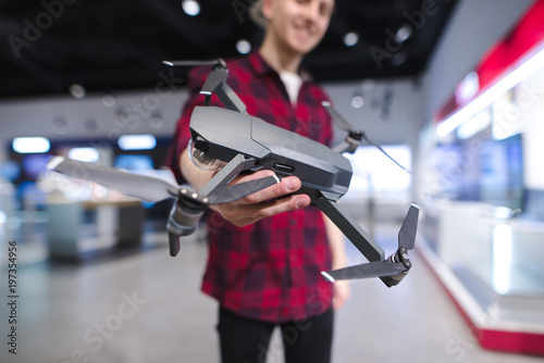 A positive young man with a quadcopter in his hands is in the drones store. Buy a dron at an electronics store