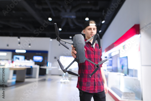 Young man holds a dron in his hands against the backdrop of a modern store. Buy quadcopter in the technology store