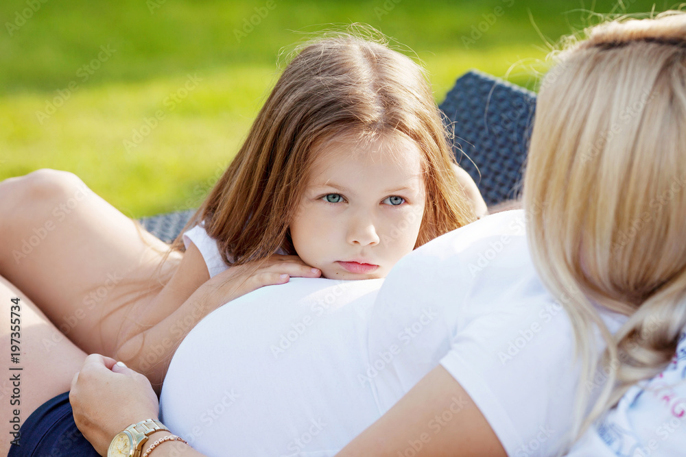 Little girl embraces a stomach of pregnant mother. Serious and thoughtful look.