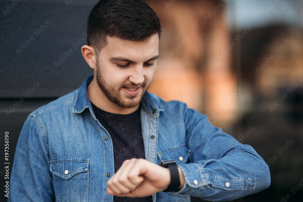 Obraz premium Handsome man in a denim shirt uses a phone standing on the street