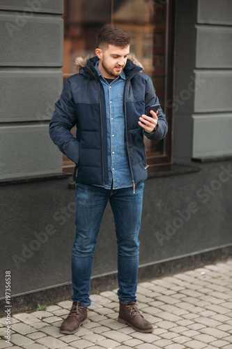 Handsome man in a jacket uses a phone standing on the street