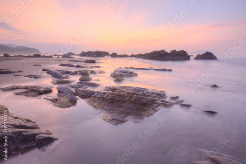 Sunrise scenery of a beautiful rocky beach on northern coast of Taiwan with an island on distant horizon under dramatic dawning sky   golden sunlight reflecting on the seawater  Long Exposure Effect 