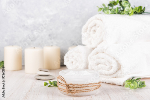Spa composition on white wooden background. Sea salt, white rolled towels, candles, green herbs