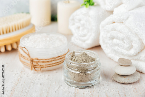 Spa composition on white wooden background. Sea salt, white rolled towels, candles, green herbs, natural clay mask for face and body.