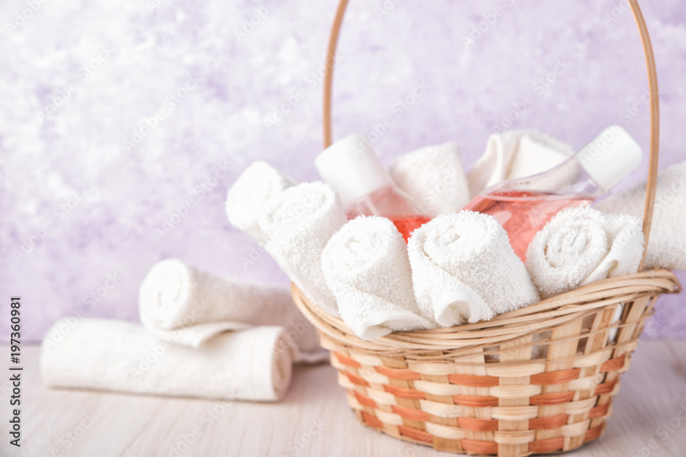 Rolled up white spa towels in a basket. Violet or purple marbel stone background. Pink lotion and shampoo. Rolled up white spa towels in a basket. Violet or purple marbel stone background. Pink lotion and shampoo.