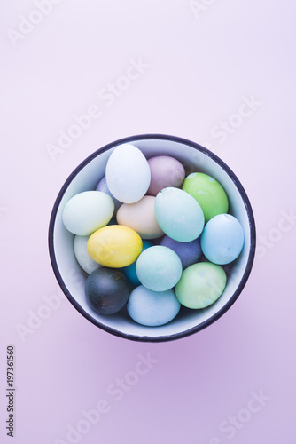 Colored eggs with pastelle tones inside a metallic bowl over a pink background, back lighted,  easter concept,holiday.