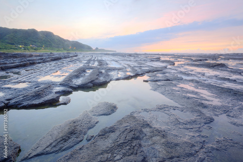 Dramatic sky  with reflections of golden sunlight on sea water and a distant island on horizon under dramatic dawning sky  Long Exposure Effect   Sunrise by the rocky coast in northern Taiwan 